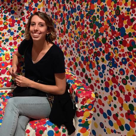 Picture of a person sitting and smiling in a room full of painted multicolor circles.